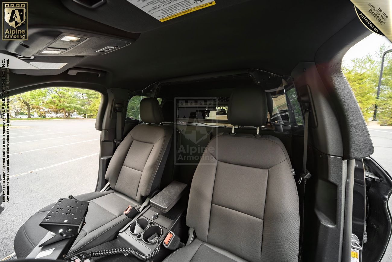 Interior of an armored Ford Explorer PPV with two front seats, a central console with equipment, and branding for Alpine Armoring visible on the dashboard and seat partition.