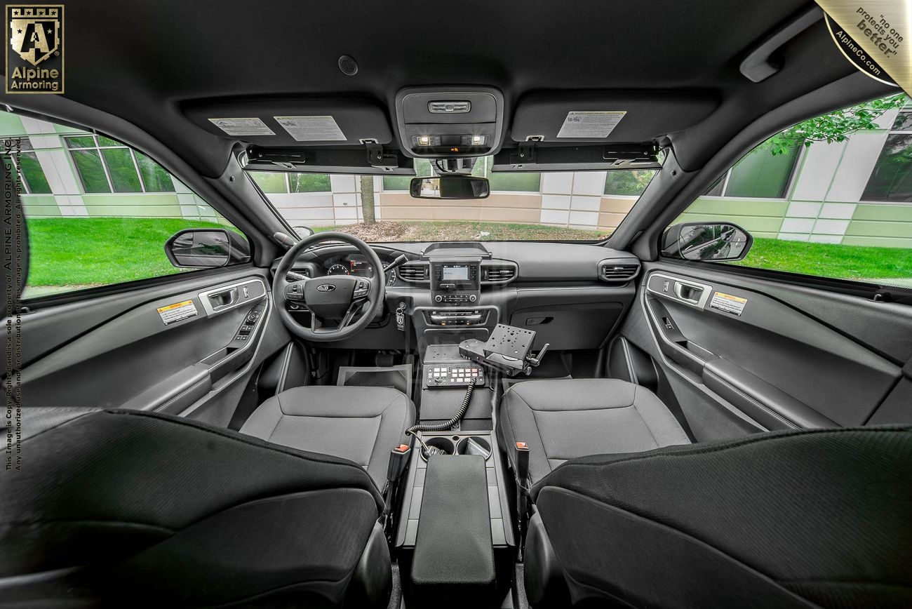 Interior view of a police vehicle (PPV), showing the front seats, dashboard, steering wheel, mounted equipment, and a partition separating the front and back seats.