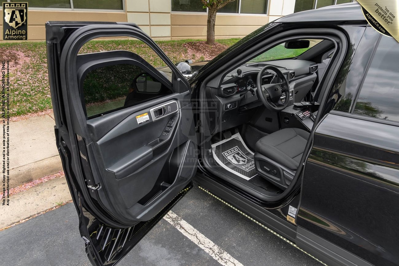 Black Police Protection Vehicle (PPV) with driver's side door open, showcasing the interior. The vehicle is parked in front of a building with a tree nearby. The dashboard, seat, and floor mat are visible.