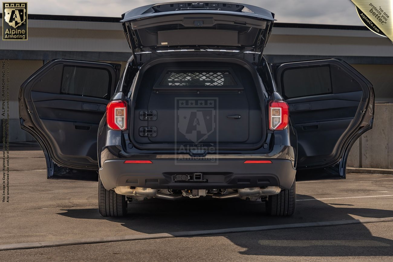 A Ford Explorer PPV with rear and side doors open, showcasing the storage and cargo area. The vehicle is in a parking area with a building in the background.