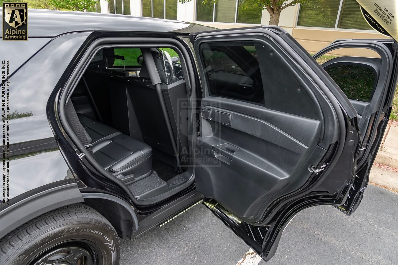 Open rear passenger door of a black PPV, showcasing its clean, black interior. The vehicle is parked on a street with a building and greenery visible in the background.