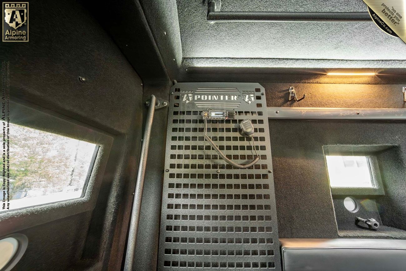 Interior view of a tactical Pointer van showing a communications device mounted on a perforated metal panel, with small windows on both sides. Alpine Armoring logo is visible in the top left corner.