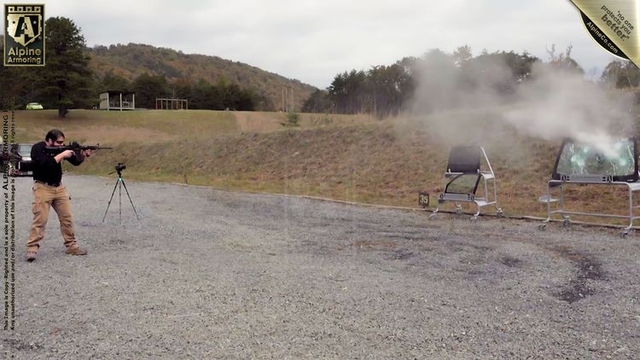 A man conducting a ballistic test by shooting at a piece of armored glass mounted on a stand at a firing range. The glass is shattering upon impact, demonstrating its resistance and durability.