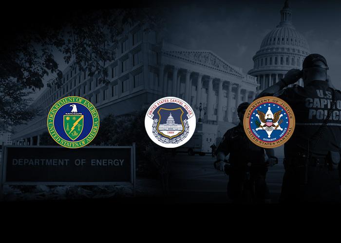 Three government seals illuminated against a dark background of the U.S. Capitol Building and a police officer. Left to right: Seal of the Department of Energy, Seal of the United States Capitol Police, and Seal of the Department of State.