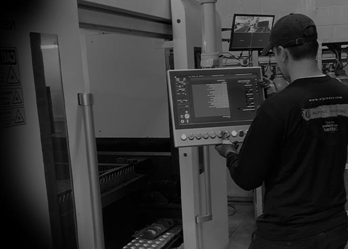 A n Alpine Armoring employee operates a large machine via a touchscreen interface in an industrial setting. Monitors and equipment are visible in the background.