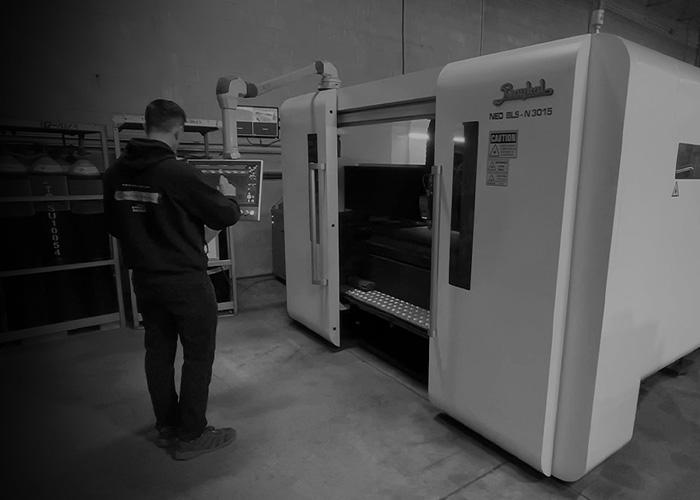 An Alpine Armoring employee operates a large industrial machine in a factory setting, focusing on the control panel.