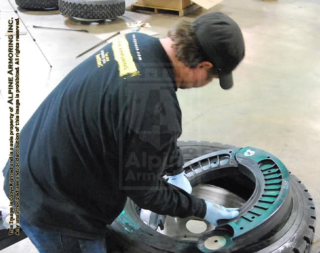 A technician at Alpine Armoring installing a run-flat tire system into a tire, showcasing the assembly process for armored vehicle components.