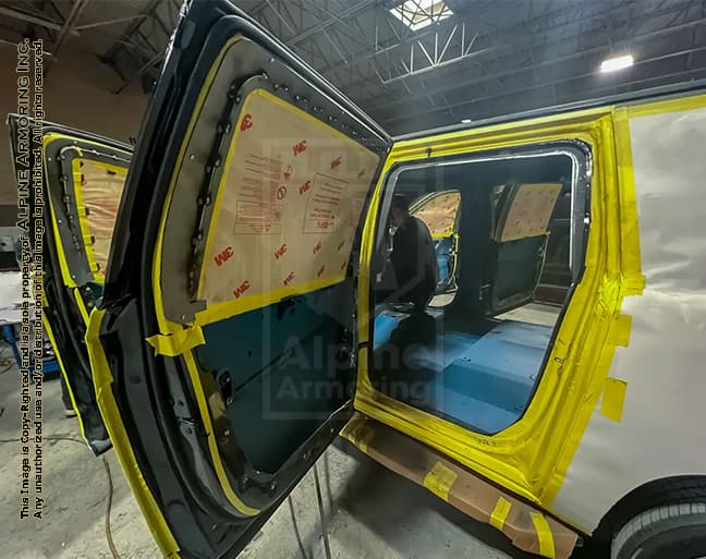 A partially dismantled vehicle with its doors open undergoing interior repairs in a workshop. Yellow tape and masking coverings protect various components during the process.