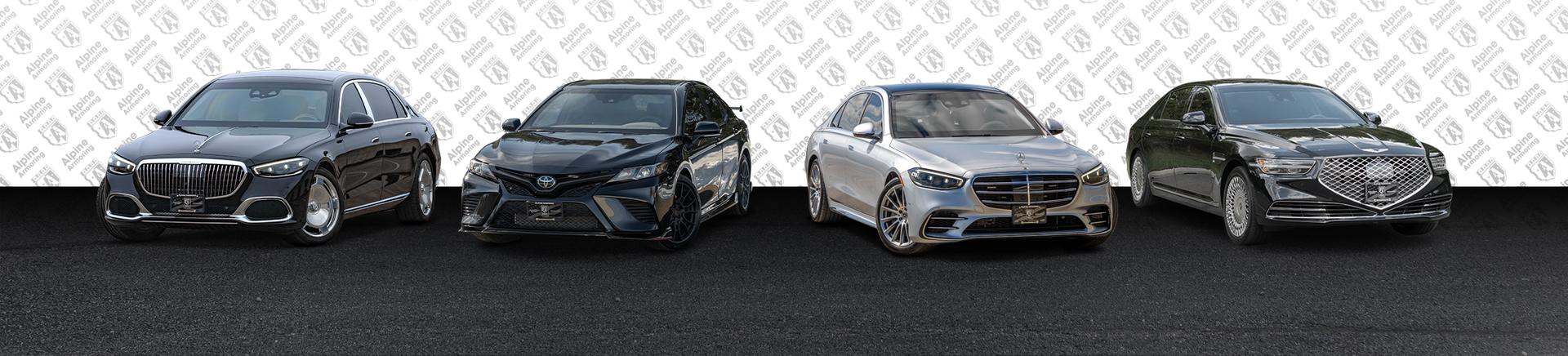 Four luxury sedans from Alpine Armoring are parked side by side against a patterned background. They vary in colors: black, dark gray, silver, and dark green, showcasing different designs and models.