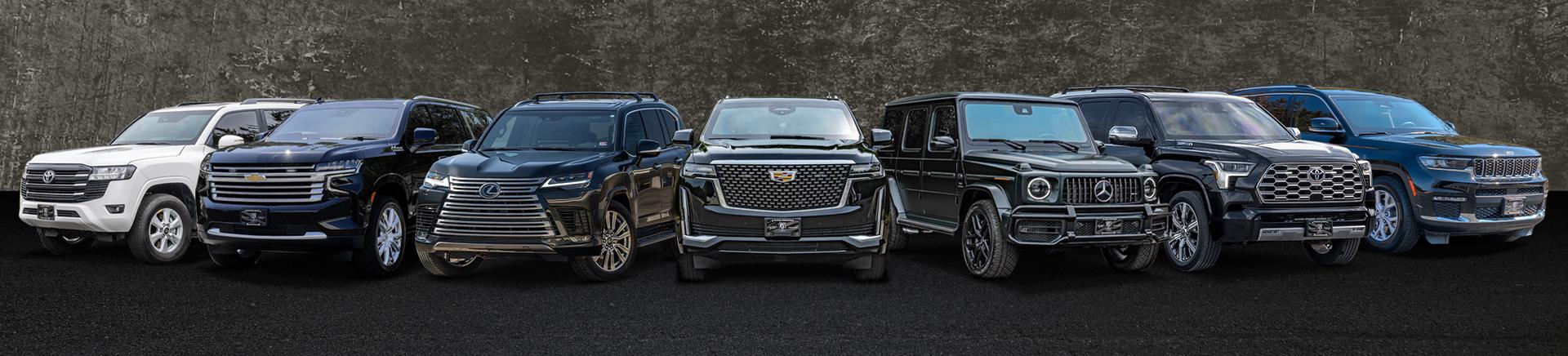  A lineup of seven luxury SUVs from Alpine Armoring in various colors, including white, black, and dark blue, parked side by side on a black road. The cars have prominent grills and sleek designs, showcasing different brands and styles.