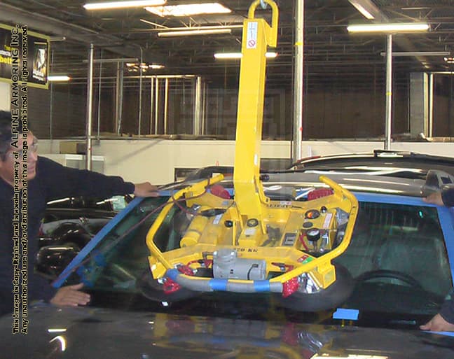 Two technicians at Alpine Armoring using a hydraulic lift to install a bulletproof windshield on an armored vehicle, showcasing the precise installation process for enhanced vehicle protection.