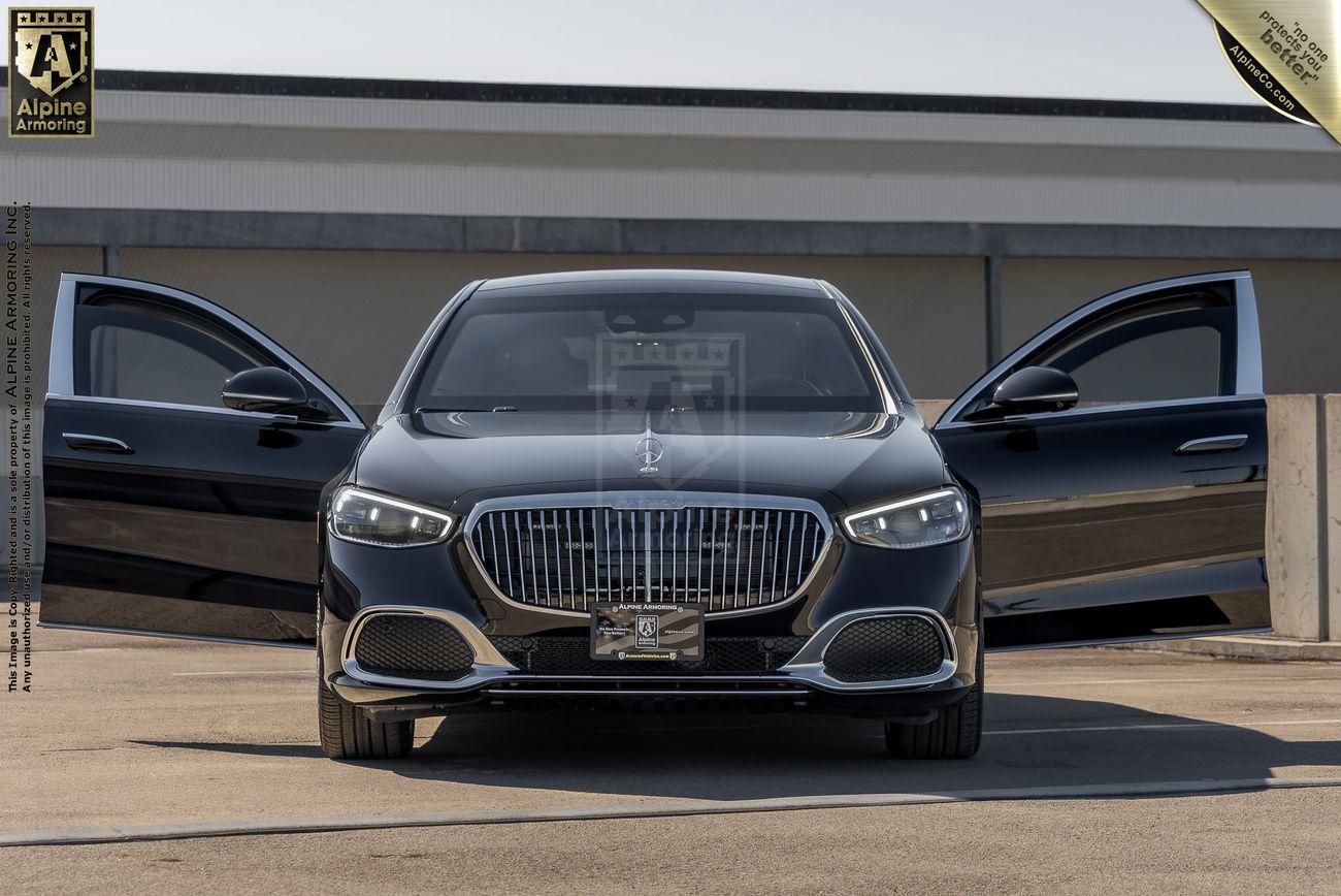 A black Mercedes-Benz S 580 Maybach sedan with both front and rear side doors open, parked on a concrete surface with a building in the background.