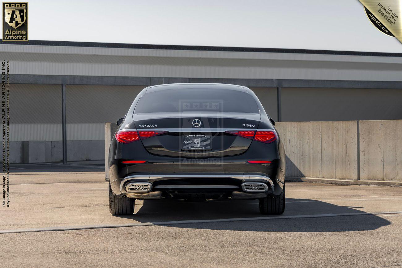 A black armored Mercedes-Benz S 580 is parked in an outdoor lot, viewed from the rear, showcasing its model badge and exhaust details.