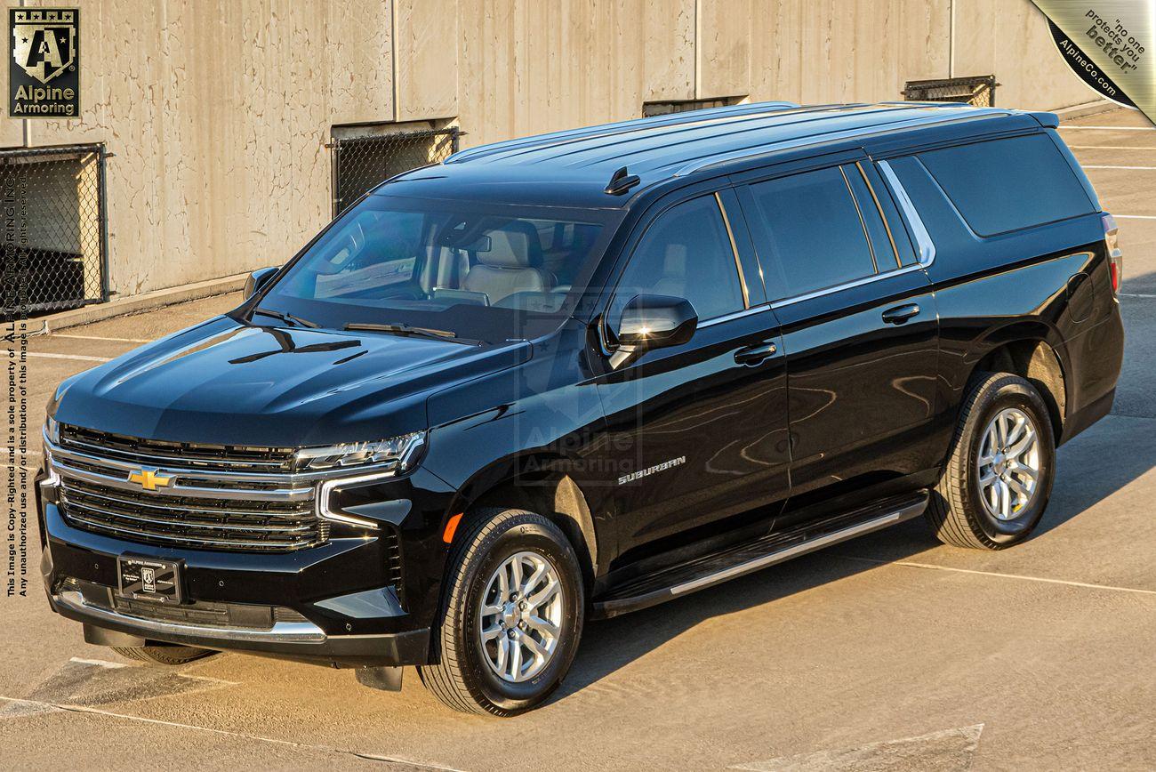 A black Chevrolet Suburban LT SUV is parked outside near a concrete wall on a sunny day.