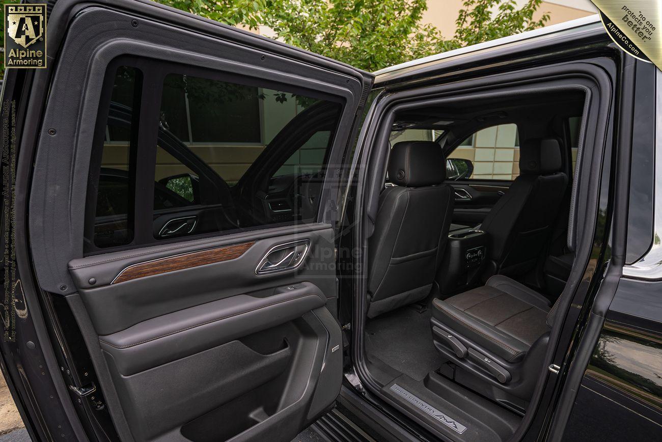 Interior of a black armored Chevrolet Suburban LT SUV with rear passenger door open showcasing black leather seating and a view of the exterior building.