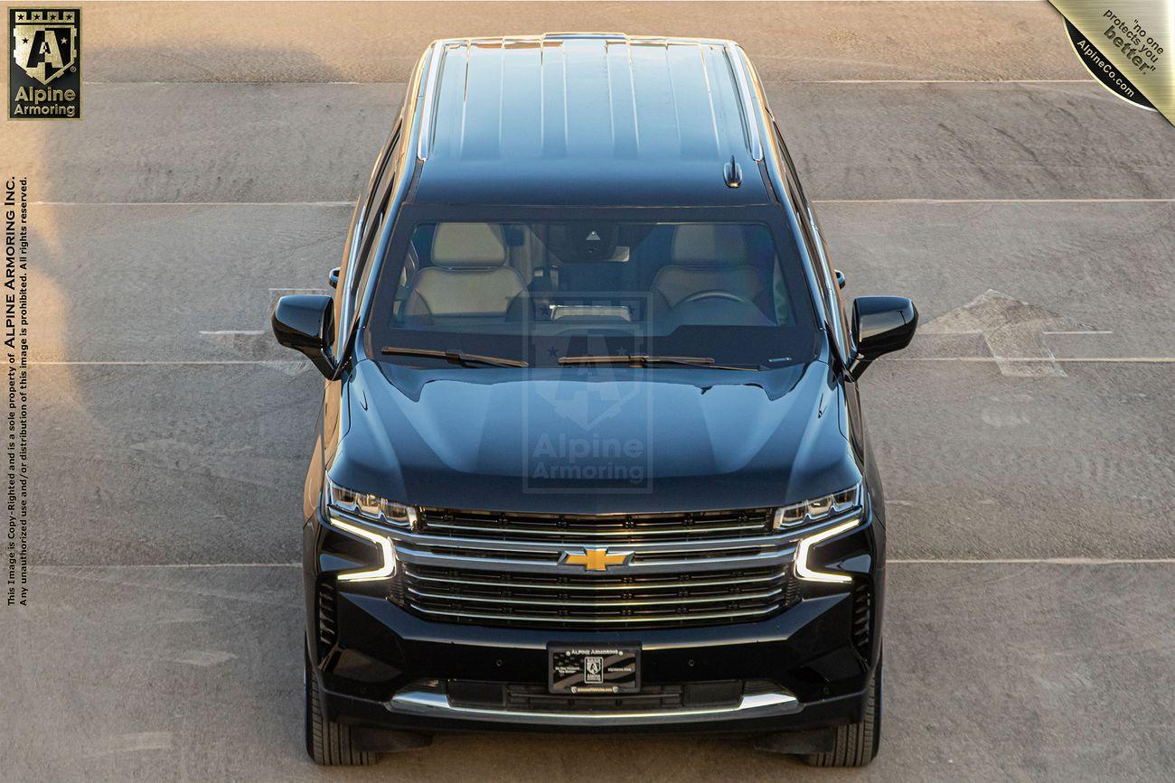 A black bulletproof Chevrolet Suburban LT SUV viewed from above, parked on a concrete surface with a visible logo on the front grille and a "2" plate on the bumper.