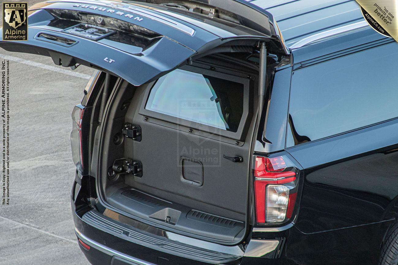 A black armored Chevrolet Suburban LT SUV with its rear door open, revealing a specialized secure storage compartment inside.