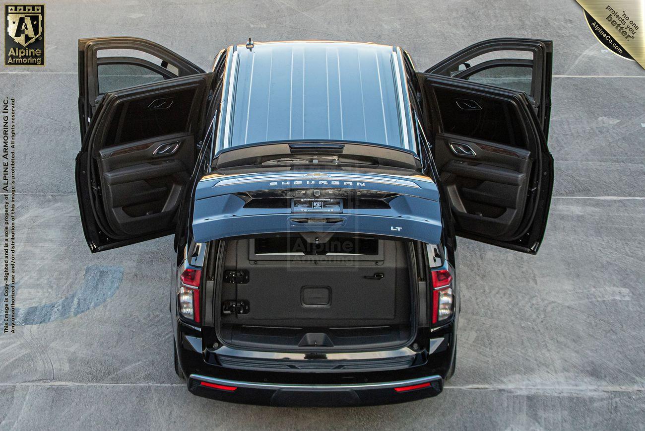 A black armored Chevrolet Suburban LT SUV with all four doors and the rear hatch open, displayed on a concrete surface. The vehicle has a sunroof and visible seats and cargo area.