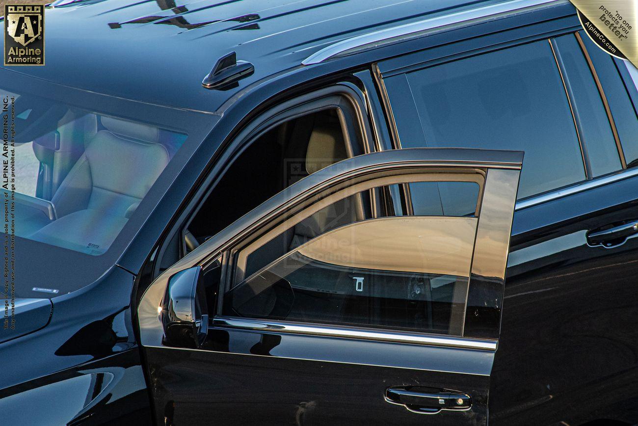 A black armored Chevrolet Suburban LT SUV with an open driver's side door, reflecting light on the glossy exterior. The interior is slightly visible through the windows.