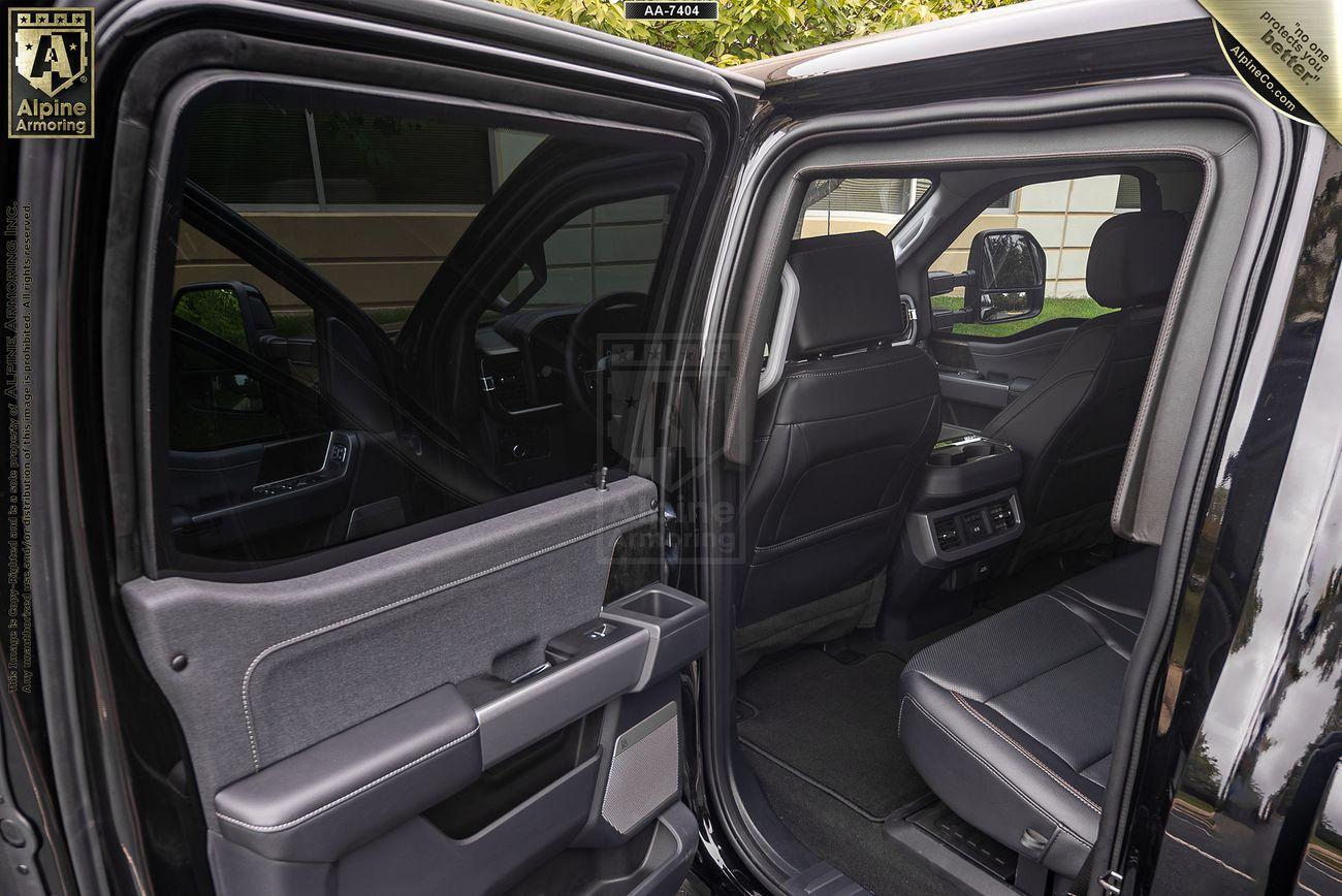 Open view of an armored Ford F-350 Lariat rear and front interior, showing black leather seats, door panels, and large windows. The rear door is open, providing a clear look into the spacious and modern cabin.