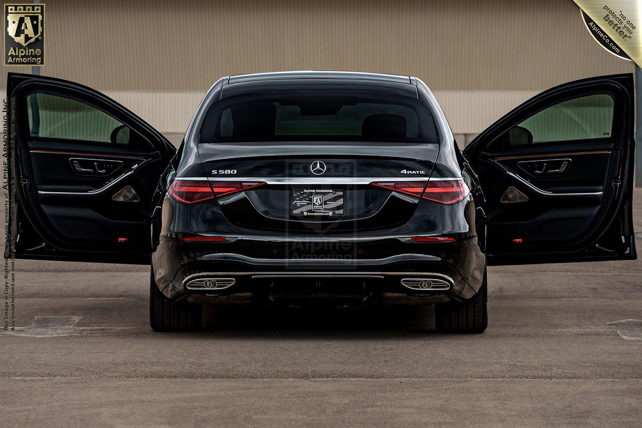 Rear view of a black Mercedes-Benz S580 with both rear doors open, parked on a concrete surface. The car features dual exhaust pipes and a visible license plate frame.