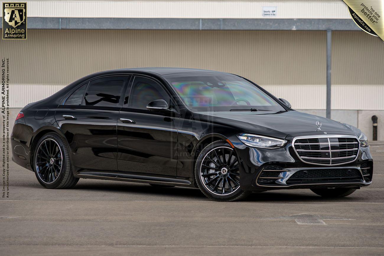 A black Mercedes-Benz S580 lucury sedan, with tinted windows and custom black wheels, is parked on a concrete surface in front of a large beige industrial building.