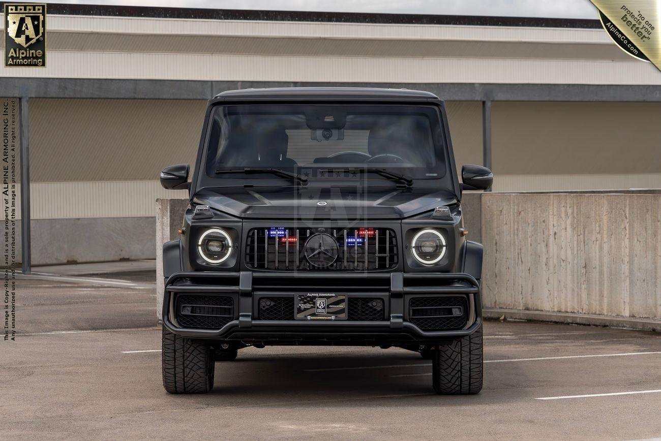 A matte black Mercedes-Benz G-Class G63 SUV is parked in an outdoor setting surrounded by autumn foliage.