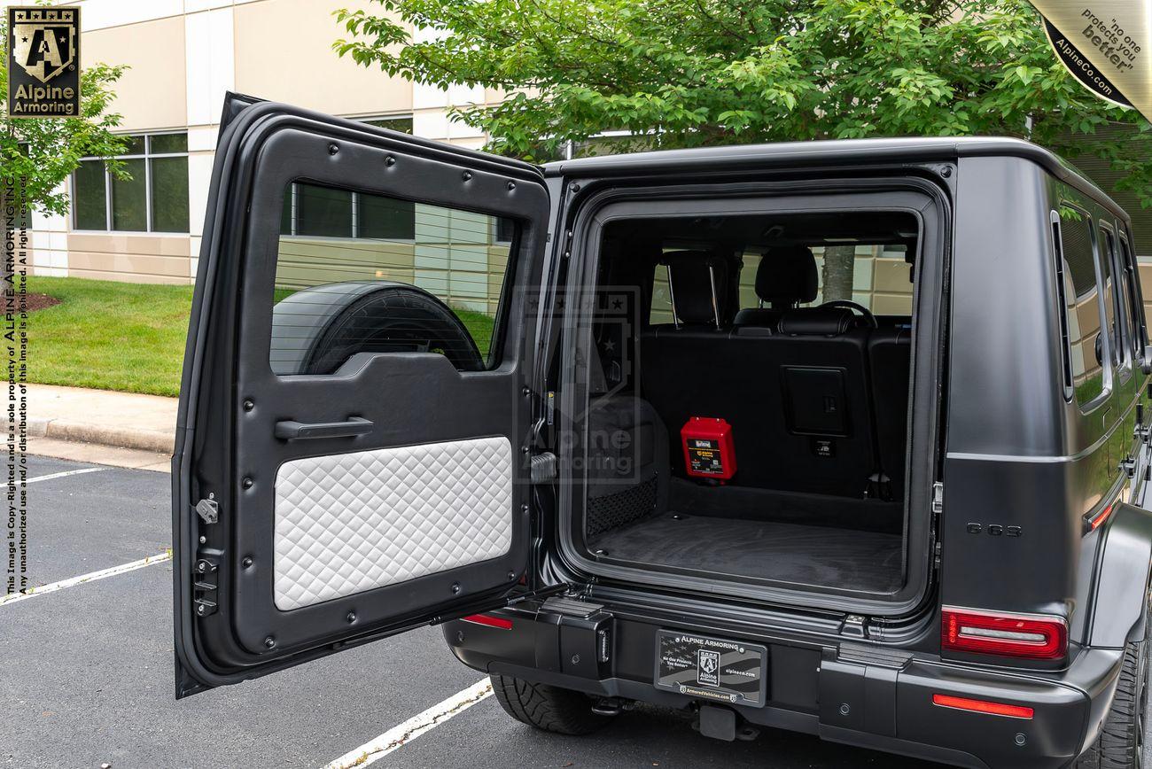 An open trunk of a black Mercedes-Benz G-Class SUV, showcasing a spacious cargo area with quilted paneling on the door, a mesh storage pocket, and a view of the backseat interior.