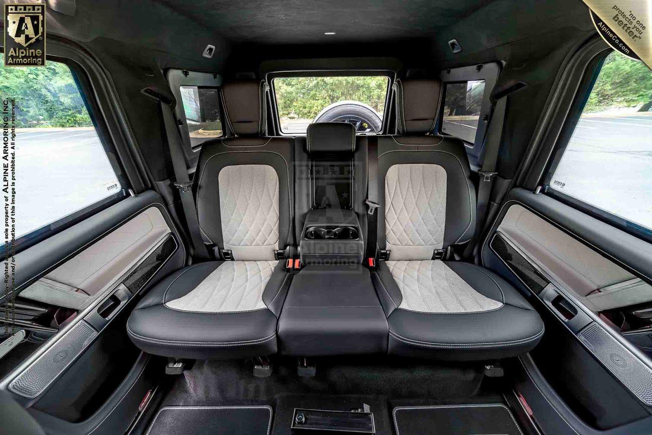 Interior view of the backseat of a G-Class SUV, featuring three leather seats with quilted patterns, two headrests, a center armrest, and windows providing an outside view.