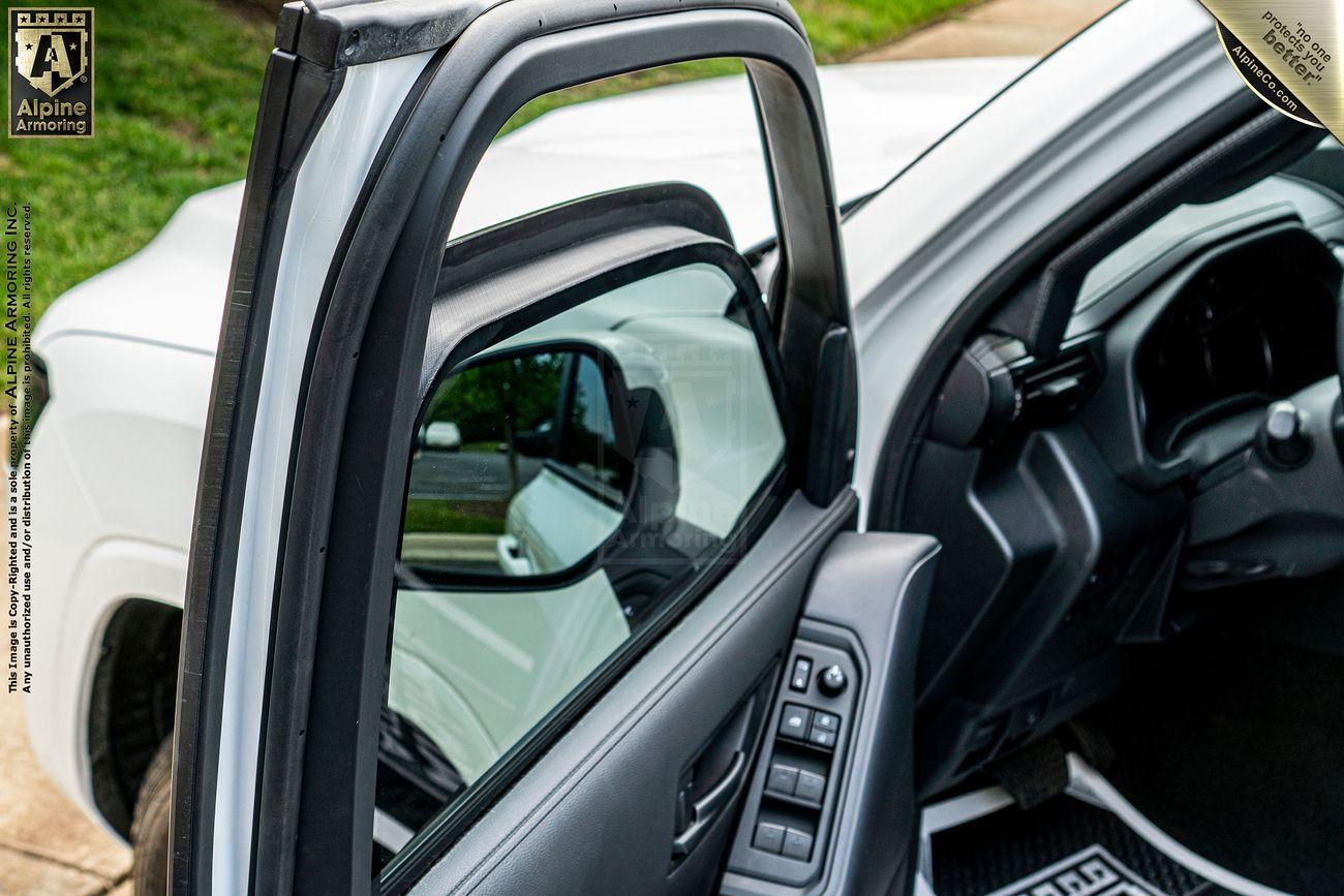 The drive door of an armored Toyota LandCruiser 300 showing a bulletproof glass window rolled partially down.