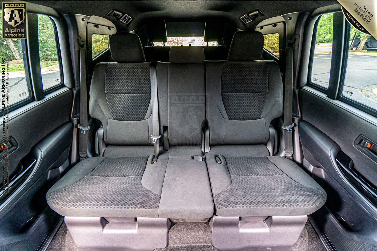 The interior of an armored Toyota LandCruiser 300  featuring three grey rear seats with headrests and seatbelts.