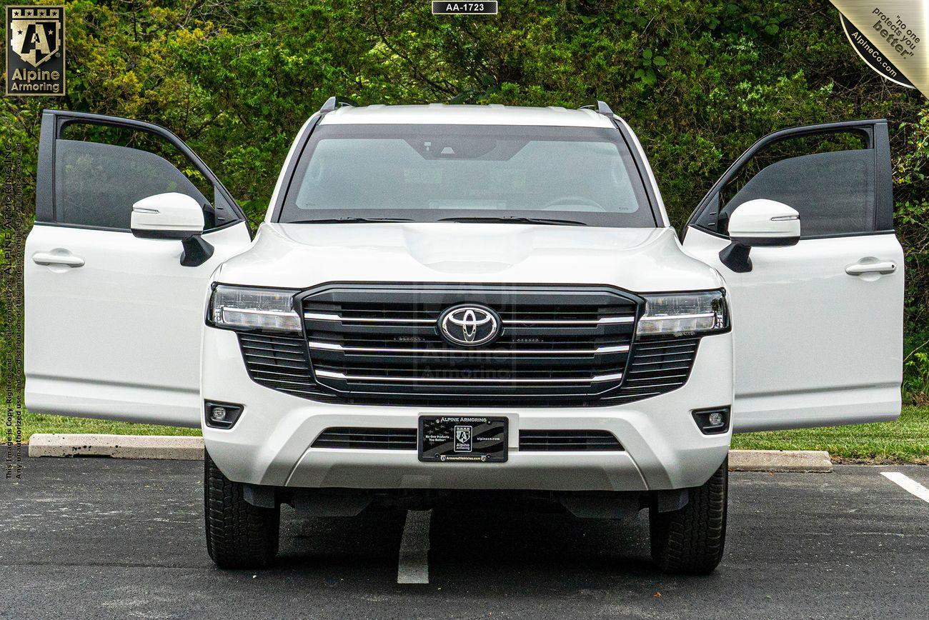 Front view of a white Toyota SUV with both front doors open, parked in an outdoor setting with greenery in the background.