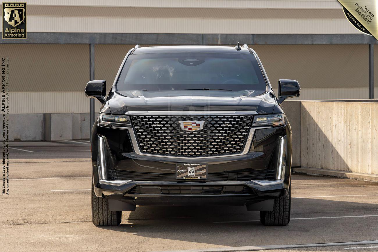 Front view of a black armored Cadillac Escalade SUV parked in an outdoor lot, with a building in the background.