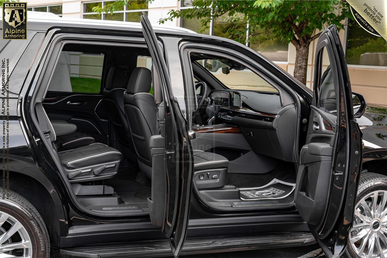 A black Cadillac Escalade SUV with all four doors open, showcasing its luxurious black leather interior, including front and rear seats, dashboard, and center console.