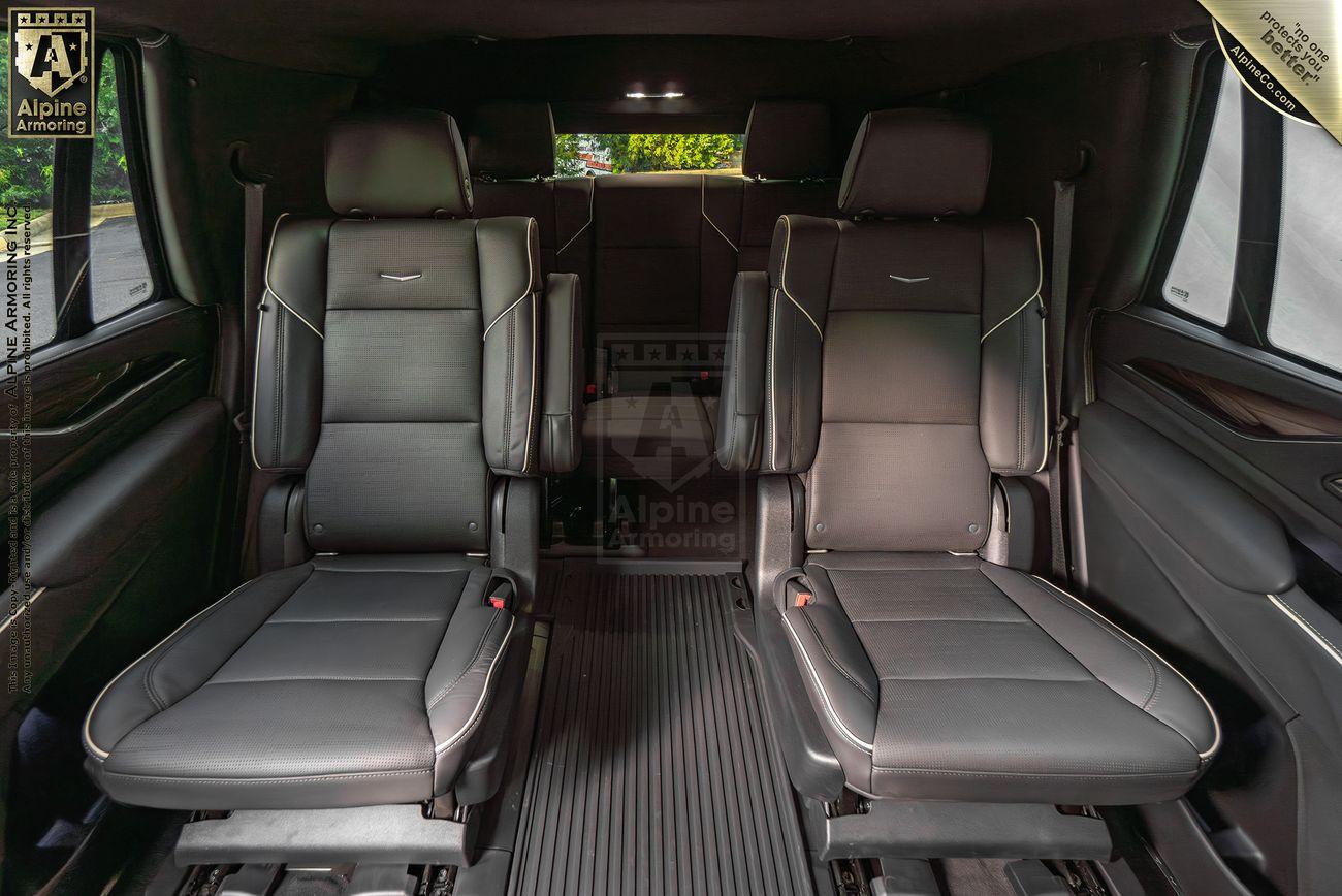 Interior view of a Cadillac Escalade SUV featuring two black leather captain's chairs with headrests and armrests, separated by an open aisle.