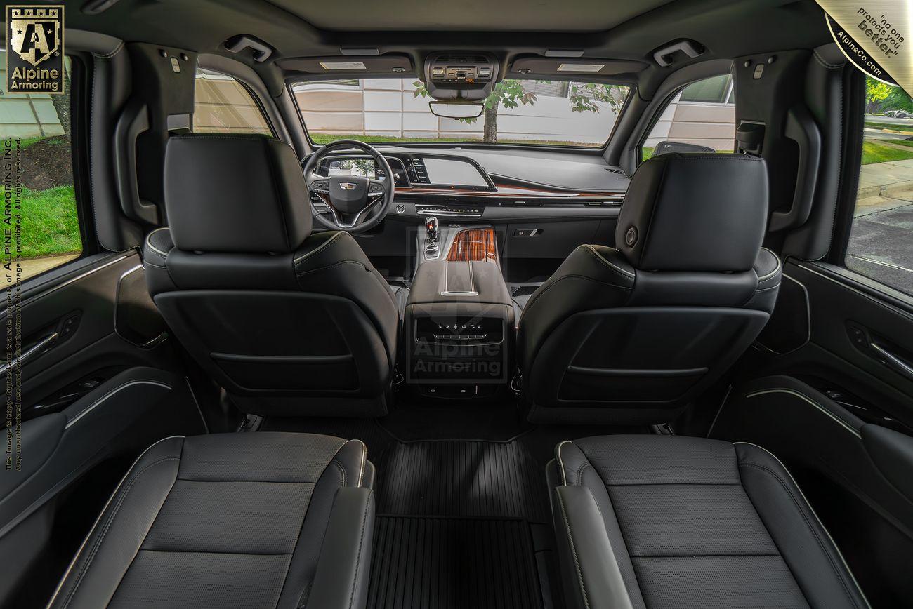 Interior view of a luxury armored Cascalade Escalade SUV vehicle showcasing the front and rear black leather seats, dashboard, and center console.