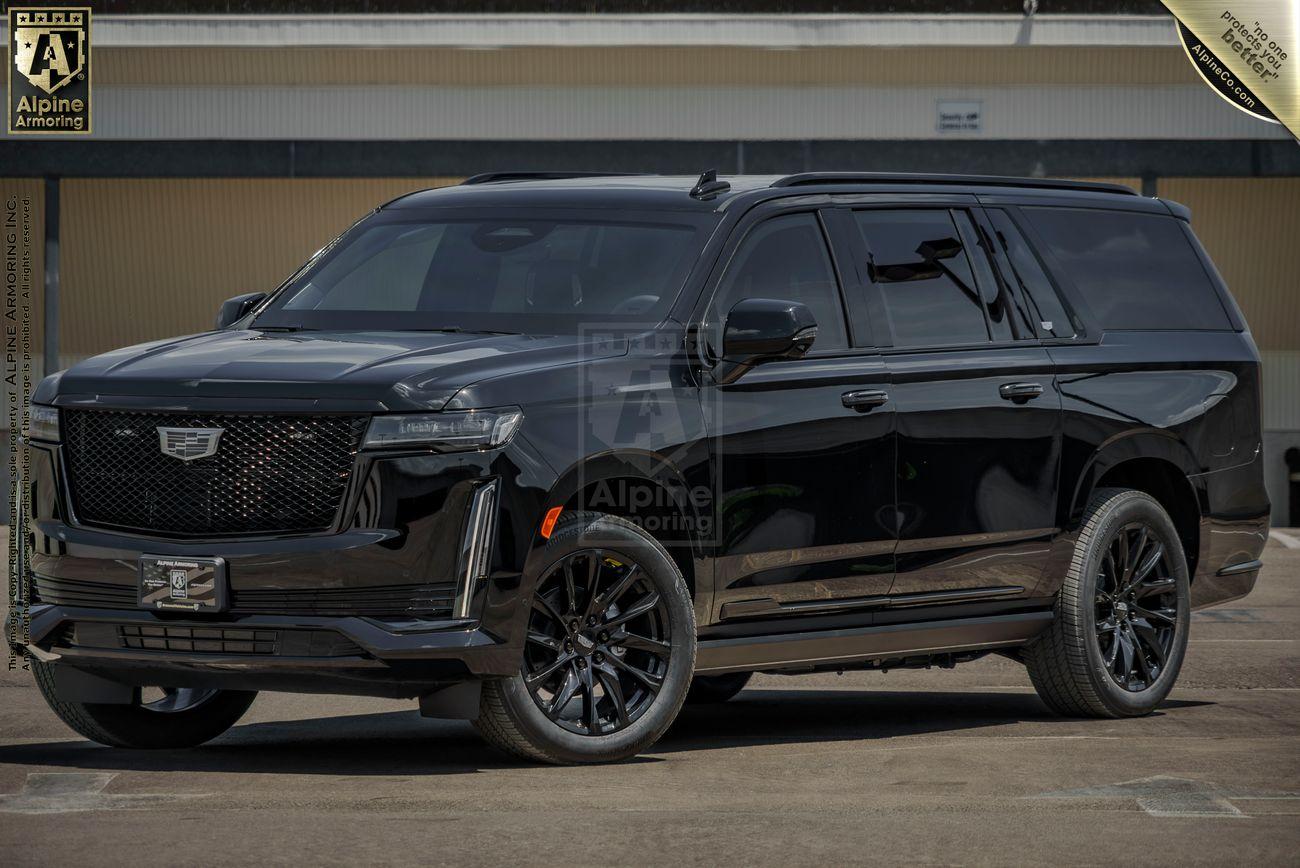 A black, full-size Cadillac Escalade ESV luxury SUV is parked on a paved area in front of a building under a cloudy sky. The vehicle is shown in a side view.