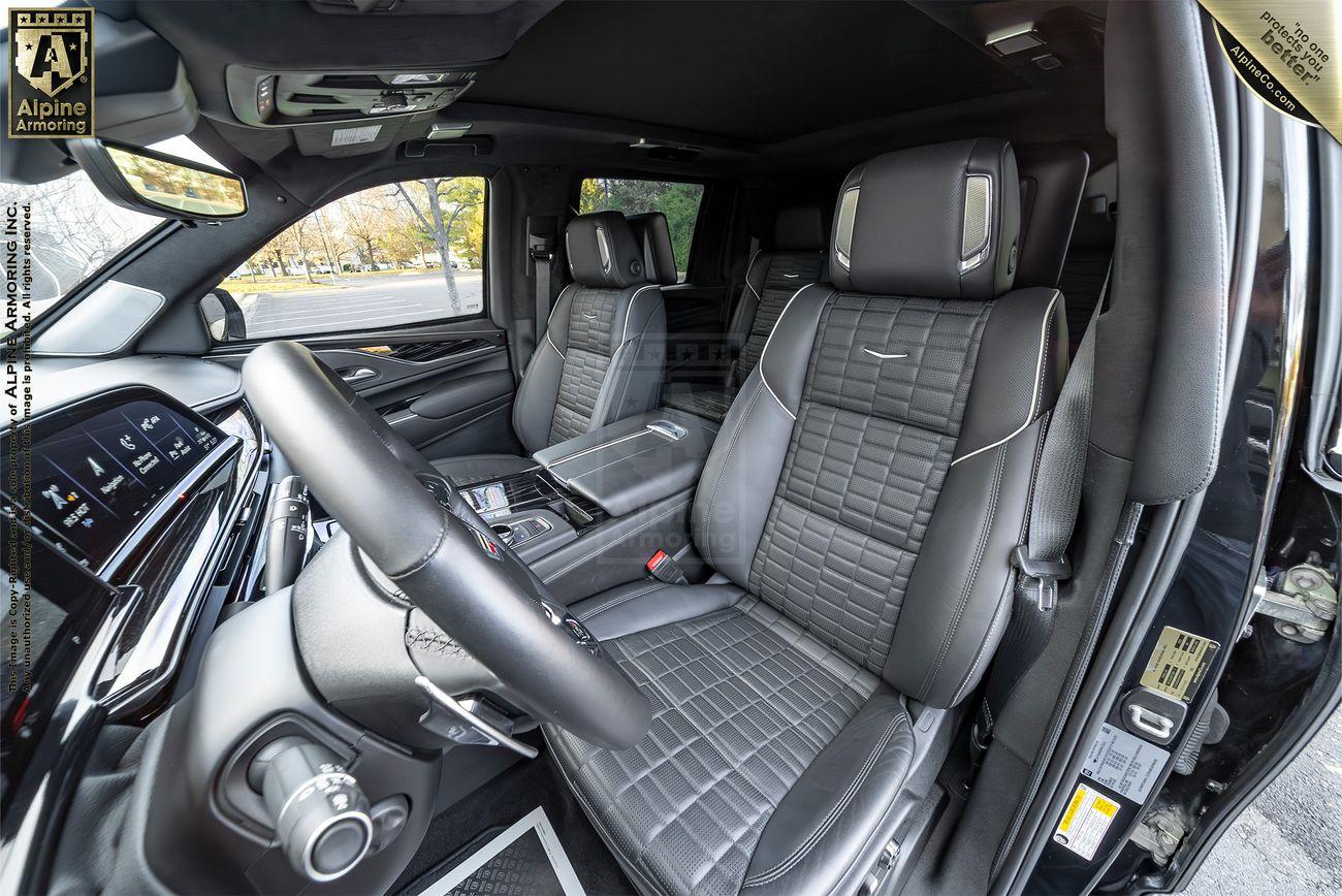 The interior of a Cadillac Escalade ESV SUV, featuring black leather seats with a quilted pattern, a large touchscreen display on the dashboard, and multiple controls on the steering wheel and center console.