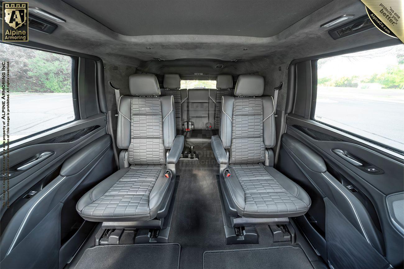 The interior of a Cadillac Escalade ESV SUV with two rows of premium leather seats, facing forward. The design appears spacious, featuring high-quality materials and ample legroom.