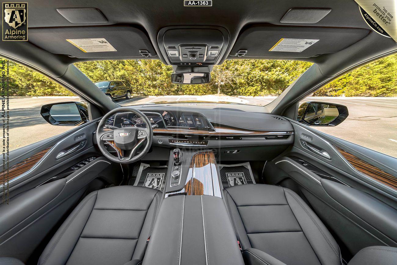 Interior view of an armored Cadillac Escalade ESV Luxury SUV showing the dashboard, steering wheel, touch screen display, wood trim, and leather seats.