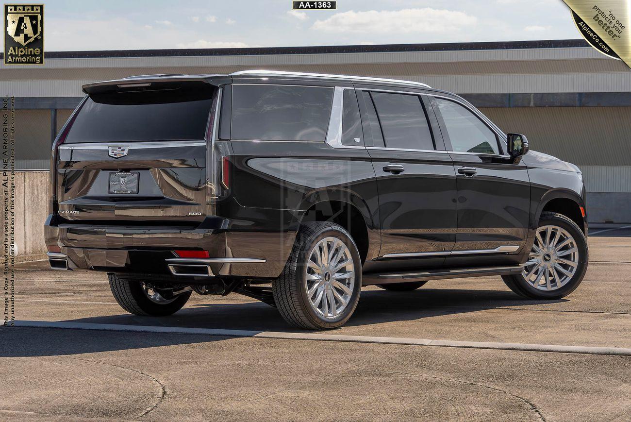 A black armored Cadillac Escalade ESV Luxury SUV is parked on an open asphalt surface, viewed from the rear and left side. The vehicle has tinted windows and polished metallic accents.