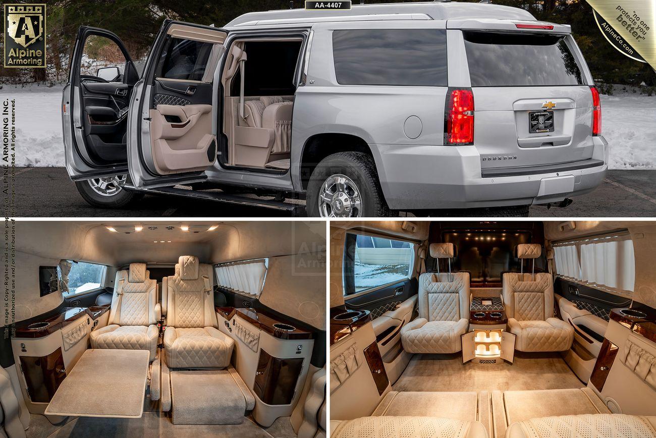 Custom Chevrolet Suburban 3500HD LT SUV with its back door open, showcasing a luxurious interior. The interior includes plush seating, tables, and advanced controls in a beige and brown color scheme.