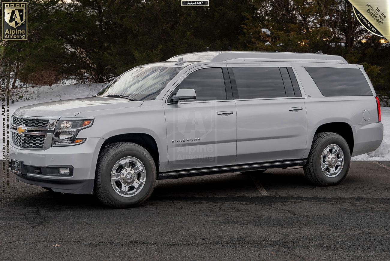 A silver armored Chevrolet Suburban 3500HD LT VIP Limo  SUV is parked on a paved area with snow and trees in the background.