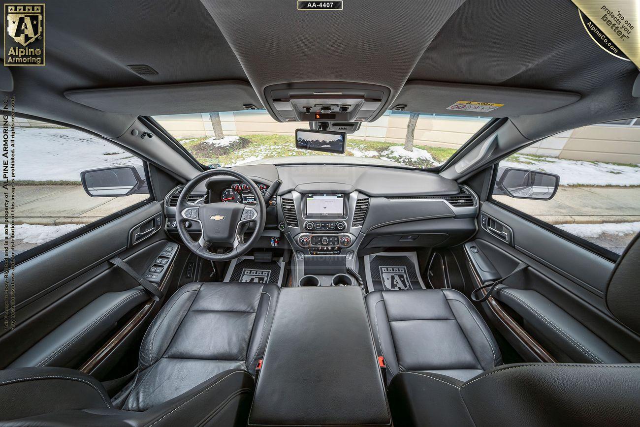 Wide-angle view of a Chevrolet Suburban 3500HD LT VIP Limo's interior featuring black leather seats, a dashboard with a central touchscreen, and a steering wheel with a visible Chevrolet logo. Snow visible outside the windows.