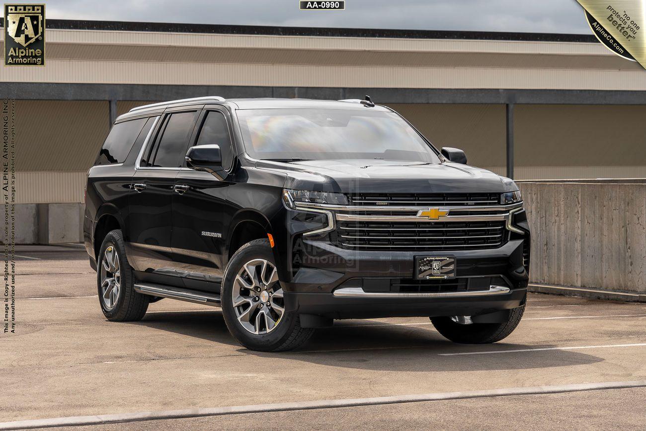 A black Chevrolet Suburban LT SUV is parked on a concrete surface in front of a building. The vehicle has a chrome front grille and alloy wheels.