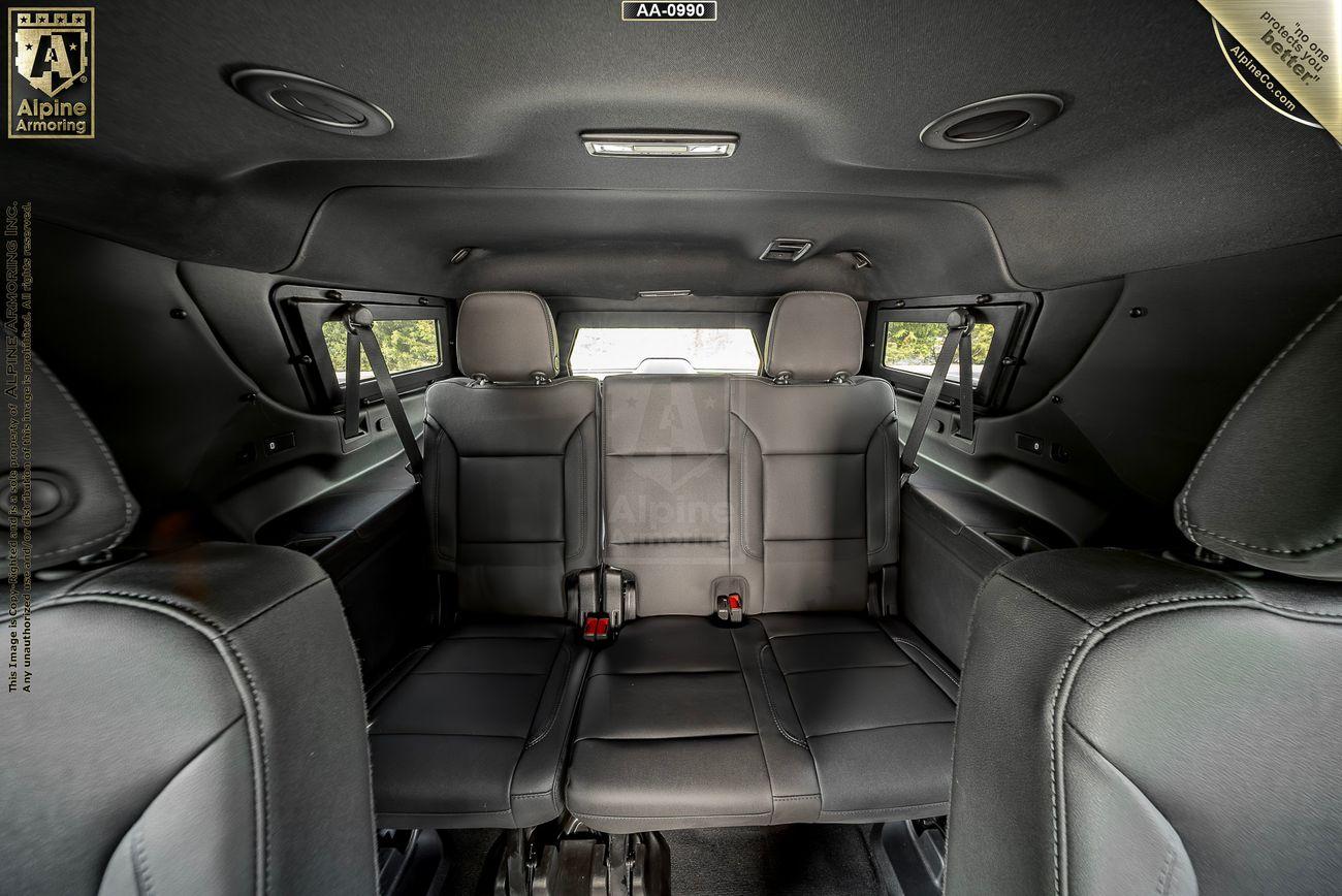 Interior view of an armored Chevrolet Suburban LT SUV showing three rows of black leather seats, seatbelt straps, and side windows.