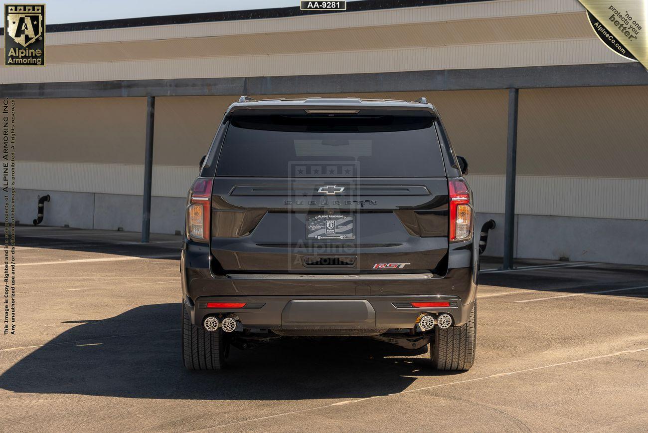 A rear view of a black armored Chevrolet Suburban RST SUV parked in an outdoor parking lot. The vehicle displays a bowtie emblem and "RST" badge on the back.