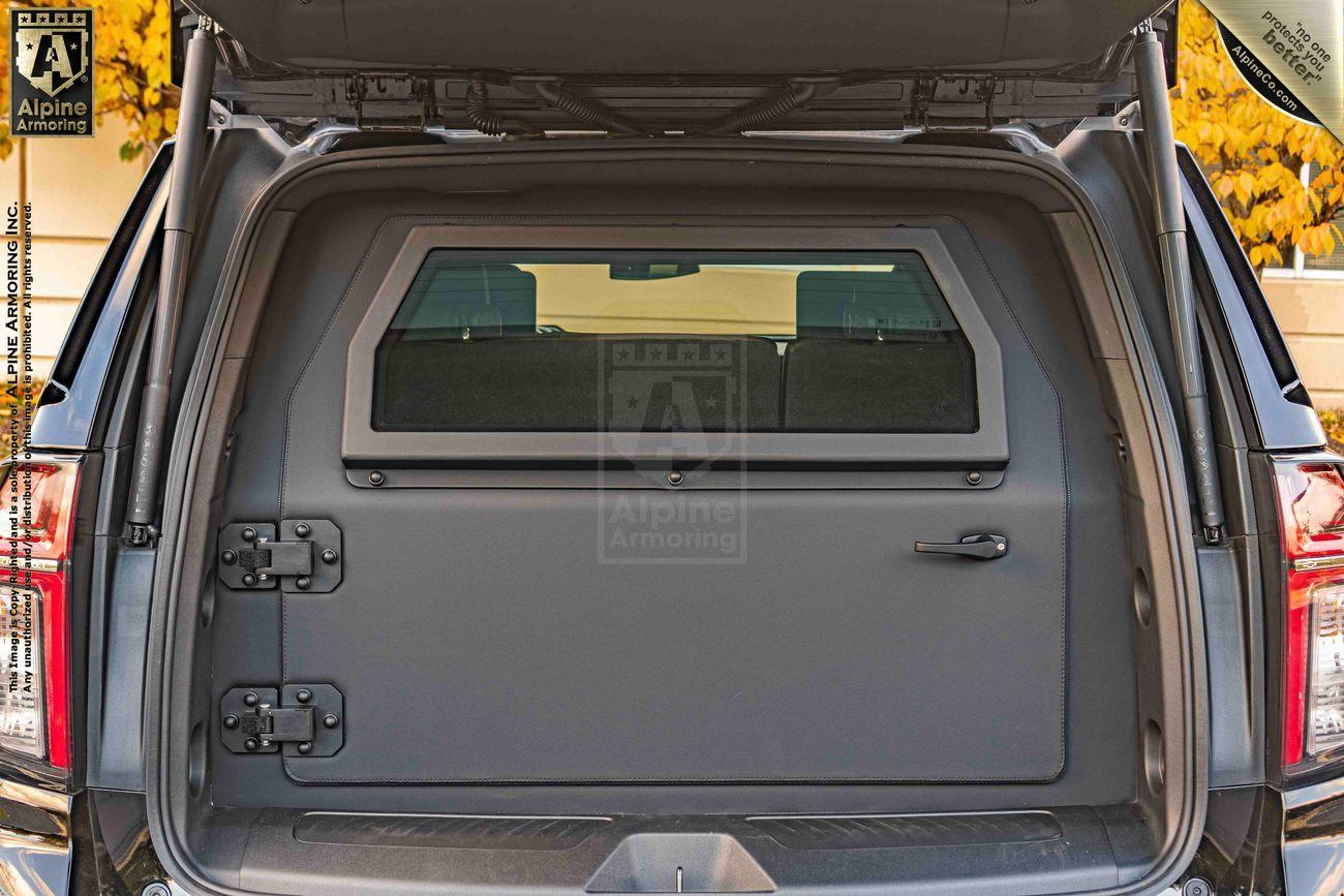 The rear interior view of an armored black Chevrolet Tahoe SUV with an open tailgate, showing reinforced hinges and door mechanisms.