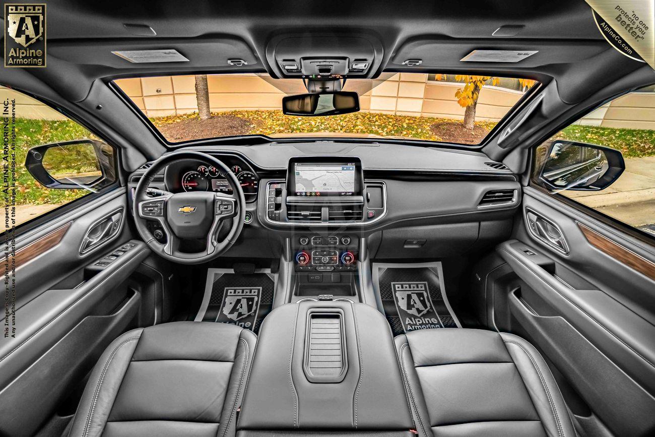 Interior view of an armored black Chevrolet Tahoe SUV with black leather seats, a digital dashboard, and a central touchscreen display. .