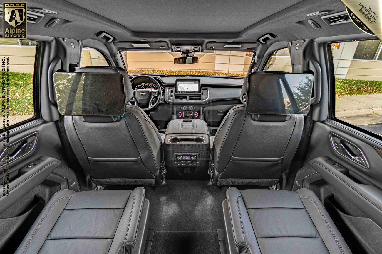 Interior view of an armored Chevrolet Tahoe SUV featuring black leather seats, mounted screens on the back of the front seats, a central dashboard with a navigation screen, and a control panel in the center console.